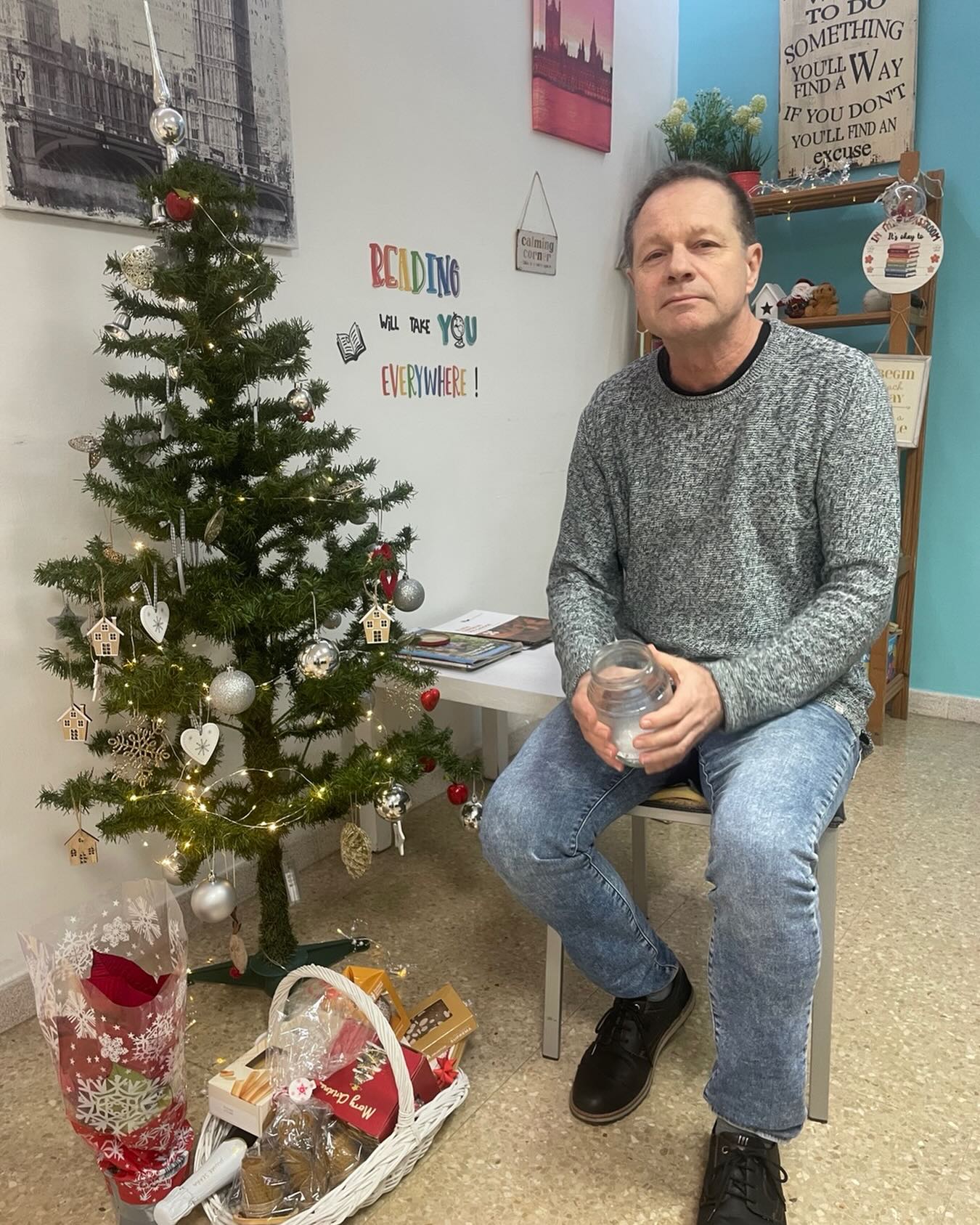 Man sitting beside a decorated Christmas tree while holding a jar during the Christmas hamper prize draw in a reading room.